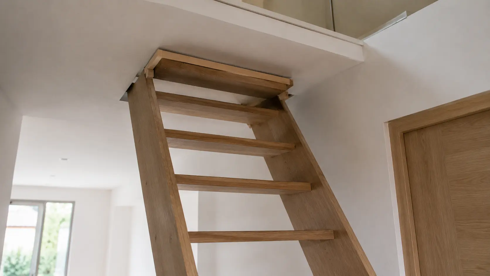 Escalier trop grand : comment le recouper sans compromettre sa sécurité Escalier intérieur en bois dont la partie supérieure arrive presque contre le plafond et ne s'aligne pas correctement avec le plancher de l'étage, illustrant un problème de hauteur de trémie dans une maison.