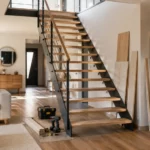 escalier intérieur ouvert sans contremarches dans une maison contemporaine, avec quelques outils et panneaux de bois au pied de l'escalier évoquant un chantier de rénovation en cours.