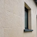 Façade de maison en pierre claire traitée avec un hydrofuge, où les gouttes de pluie perlent et ruissellent à la surface sans pénétrer le matériau.