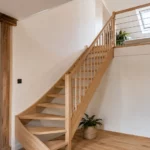 Escalier pour combles : le guide technique pour concevoir un accès sûr et confortable Escalier en bois quart tournant reliant le rez-de-chaussée à des combles aménagés lumineux avec garde-corps sobre, trémie apparente et fenêtre de toit.