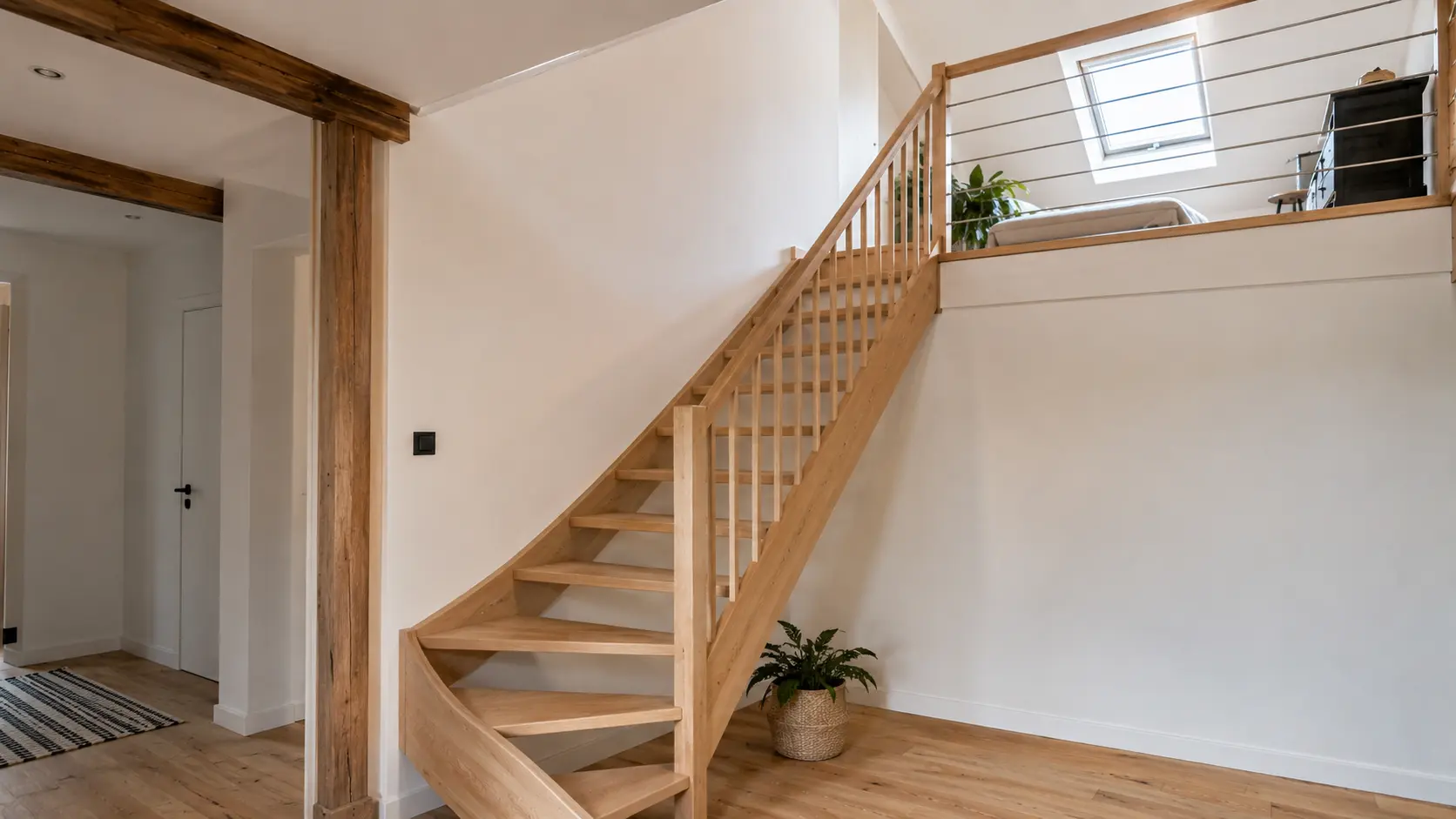 Escalier en bois quart tournant reliant le rez-de-chaussée à des combles aménagés lumineux avec garde-corps sobre, trémie apparente et fenêtre de toit.