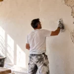 Artisan appliquant un enduit à la chaux à la truelle sur un mur intérieur en pierre